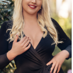 stephanie blondes escort berlin in einem schwarzen kleid, ihre langen blonden haare sind offen und wellig